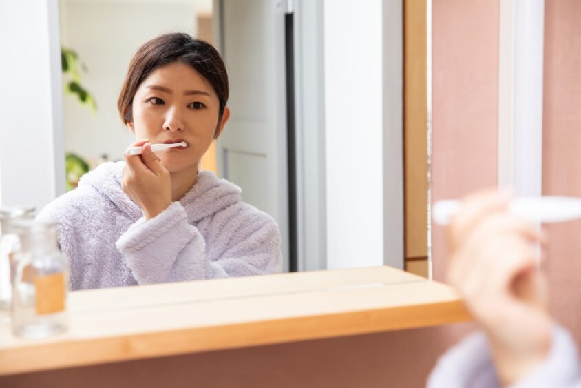 洗面台の鏡に映った歯を磨く女性